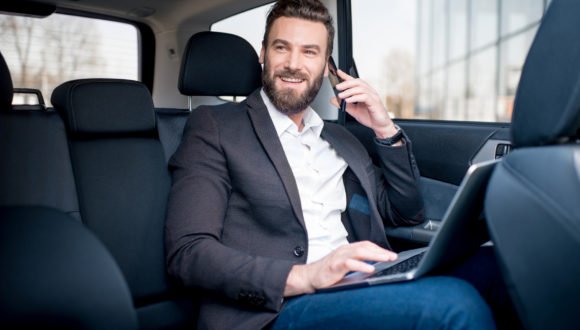 Businessman in the car Handsome businessman talking with phone sitting with laptop on the backseat of the car